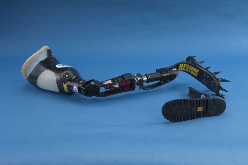 An artificial leg fitted with a claw-cleat attachment, and a boot-tread attachment lying beside.